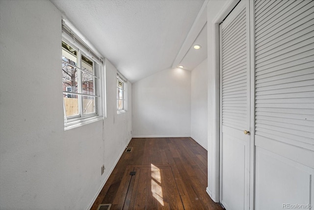 hall with a textured ceiling, visible vents, hardwood / wood-style flooring, baseboards, and vaulted ceiling