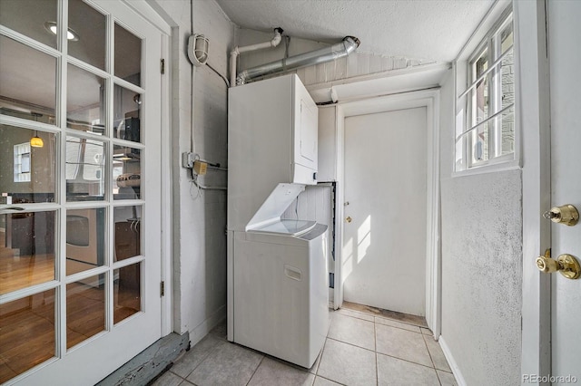 clothes washing area featuring light tile patterned floors, stacked washing maching and dryer, laundry area, and a textured ceiling