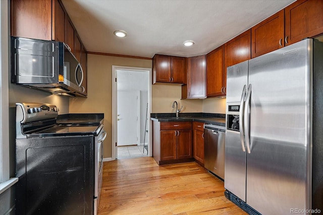 kitchen featuring a sink, light wood-type flooring, stainless steel appliances, dark countertops, and recessed lighting