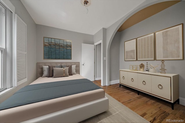 bedroom with baseboards, arched walkways, and wood finished floors