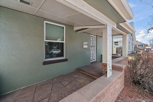 view of exterior entry featuring covered porch and stucco siding