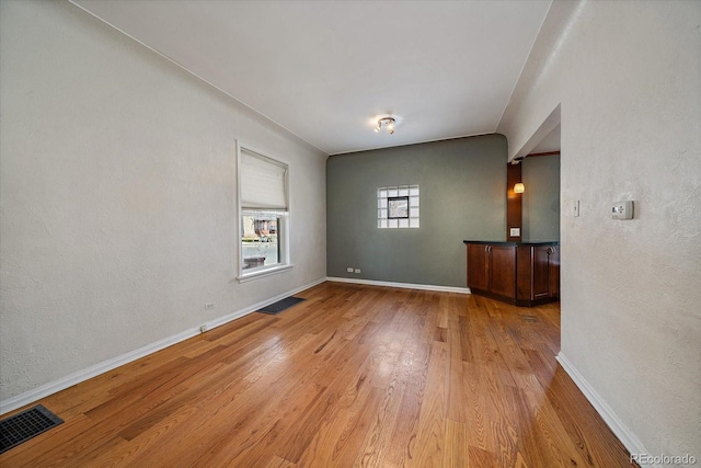 empty room featuring light wood-type flooring, baseboards, and visible vents