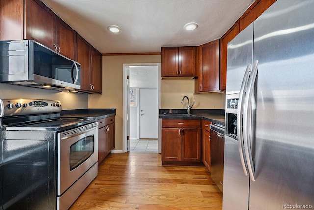 kitchen featuring a sink, appliances with stainless steel finishes, dark countertops, light wood-style floors, and recessed lighting