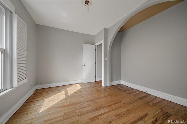 spare room featuring arched walkways, baseboards, and light wood-style floors
