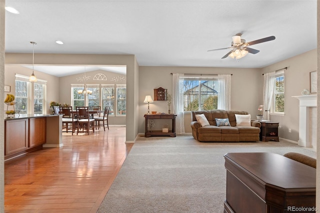 living room featuring lofted ceiling, ceiling fan with notable chandelier, and light wood-type flooring