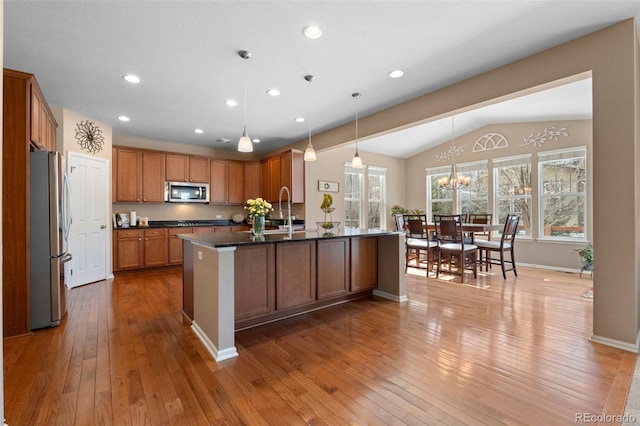 kitchen with an island with sink, appliances with stainless steel finishes, sink, and light wood-type flooring