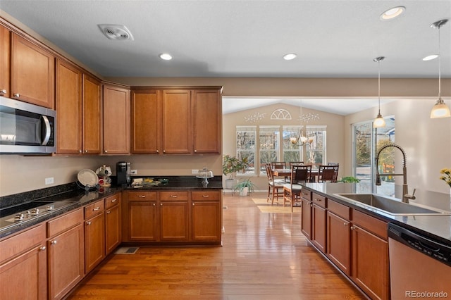 kitchen with pendant lighting, lofted ceiling, sink, stainless steel appliances, and light hardwood / wood-style flooring