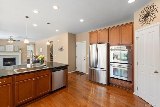 kitchen featuring appliances with stainless steel finishes, hardwood / wood-style floors, pendant lighting, sink, and a tiled fireplace