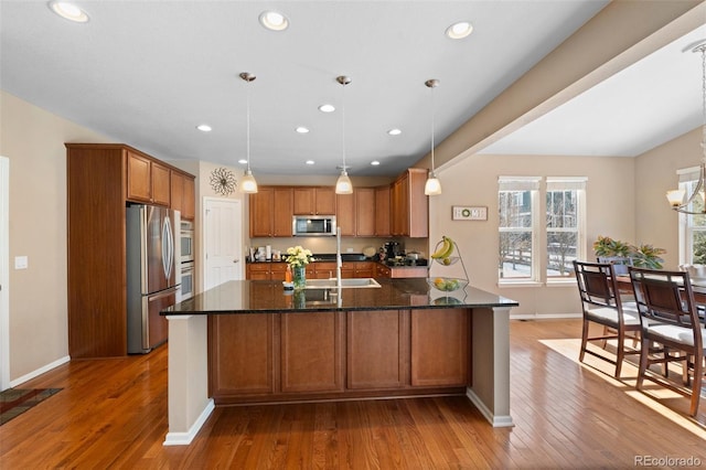 kitchen with sink, dark stone countertops, hanging light fixtures, hardwood / wood-style floors, and stainless steel appliances