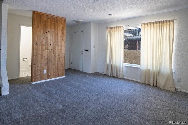 unfurnished bedroom featuring a textured ceiling, wood walls, carpet, and baseboards