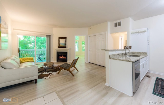 2428 W 82nd Pl Unit 3G, Westminster, CO 80031 - kitchen with stainless steel dishwasher, open floor plan, light stone countertops, a warm lit fireplace, and light wood-type flooring
