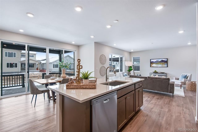 kitchen with stainless steel dishwasher, sink, a center island with sink, and light wood-type flooring