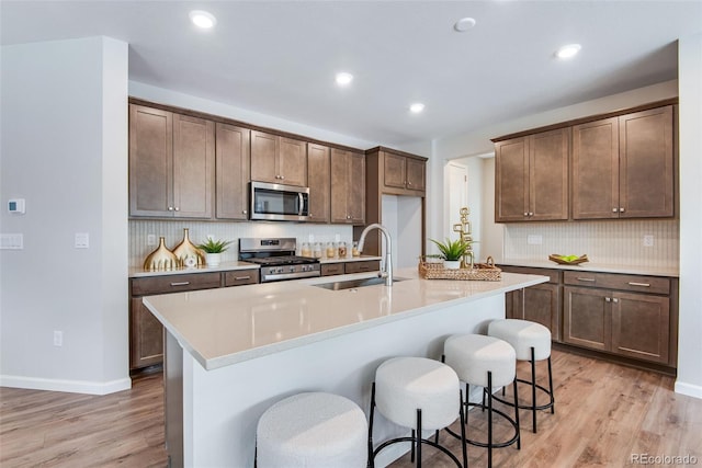 kitchen featuring an island with sink, appliances with stainless steel finishes, sink, and light wood-type flooring