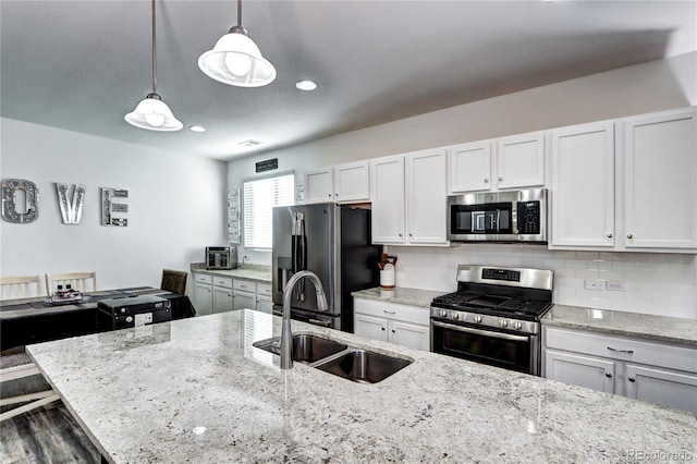 kitchen with tasteful backsplash, white cabinets, stainless steel appliances, pendant lighting, and a sink