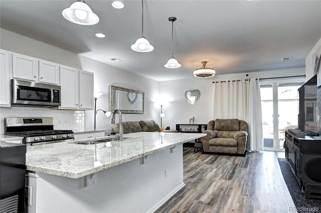 kitchen with tasteful backsplash, open floor plan, light stone countertops, stainless steel appliances, and a sink