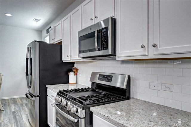 kitchen with decorative backsplash, white cabinets, appliances with stainless steel finishes, light stone counters, and wood finished floors