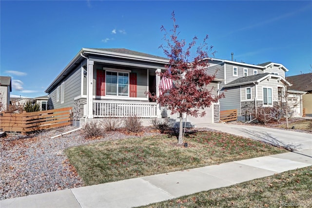 view of front of house featuring an attached garage, covered porch, fence, driveway, and stone siding