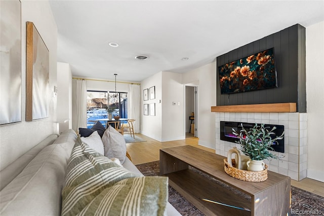 living room featuring a tile fireplace, light hardwood / wood-style floors, and an inviting chandelier