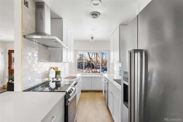 kitchen featuring decorative backsplash, wall chimney exhaust hood, stainless steel appliances, light hardwood / wood-style flooring, and white cabinets