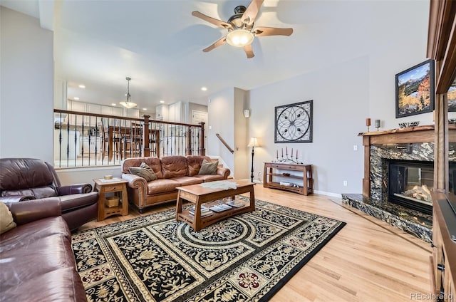 living room with ceiling fan, wood finished floors, baseboards, a fireplace, and stairway