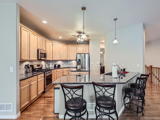 13385 Jasmine St, Thornton, CO 80602 - kitchen with appliances with stainless steel finishes, ceiling fan, a breakfast bar, light brown cabinets, and wood finished floors