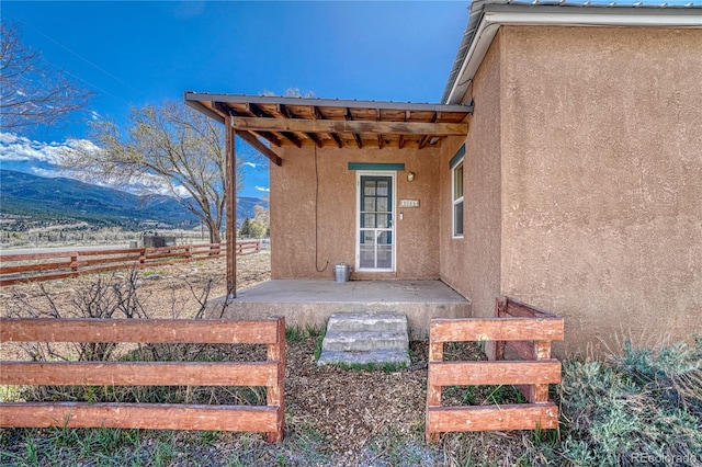 property entrance featuring a mountain view, stucco siding, fence, and metal roof