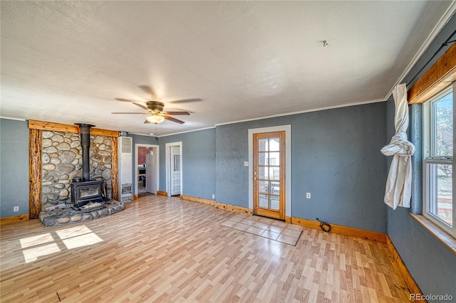 unfurnished living room featuring baseboards, a wealth of natural light, and a wood stove