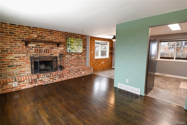 unfurnished living room with hardwood / wood-style floors, a brick fireplace, and a wealth of natural light