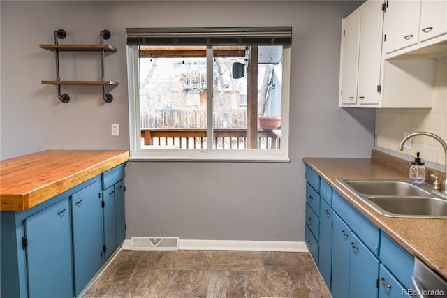 kitchen with blue cabinets, dishwasher, butcher block counters, sink, and white cabinets