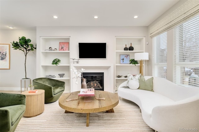 living area featuring a glass covered fireplace, built in features, and recessed lighting