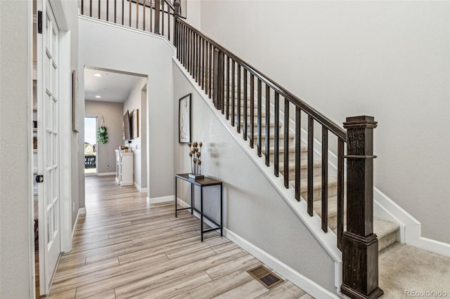 stairs with a towering ceiling, wood finished floors, visible vents, and baseboards