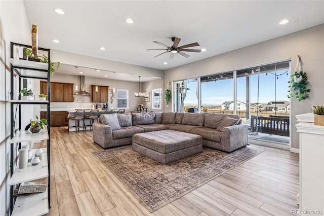 living room featuring ceiling fan with notable chandelier, light wood-type flooring, and recessed lighting