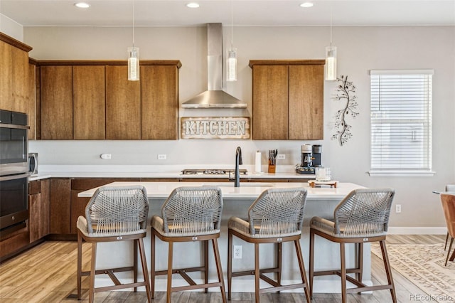 kitchen featuring brown cabinets, light countertops, stainless steel oven, and wall chimney range hood