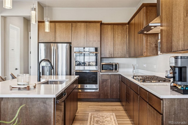 kitchen with stainless steel appliances, a sink, light wood-style floors, light countertops, and wall chimney range hood