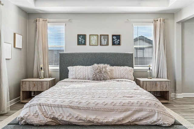 bedroom featuring a tray ceiling, wood finished floors, and baseboards