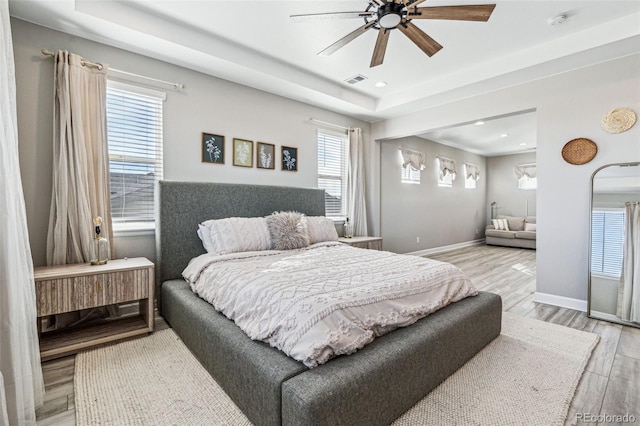 bedroom with light wood-style floors, visible vents, baseboards, and a raised ceiling