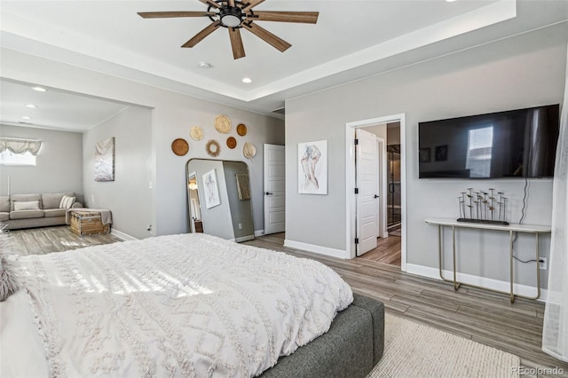 bedroom with arched walkways, recessed lighting, wood finished floors, baseboards, and a tray ceiling