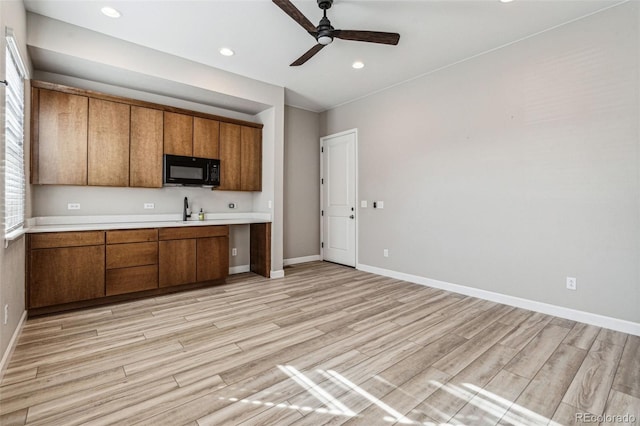 kitchen featuring light wood finished floors, black microwave, brown cabinetry, and light countertops