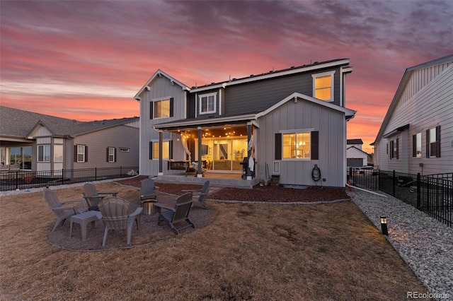 back of property at dusk featuring a patio area, a fenced backyard, a fire pit, and board and batten siding