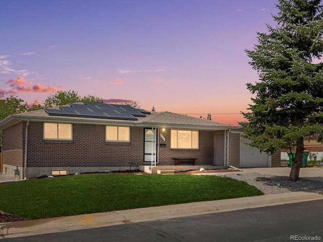 ranch-style house featuring a lawn, solar panels, brick siding, an attached garage, and driveway