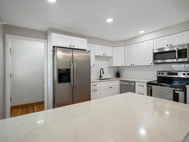 kitchen featuring appliances with stainless steel finishes, a sink, light stone countertops, decorative backsplash, and white cabinetry