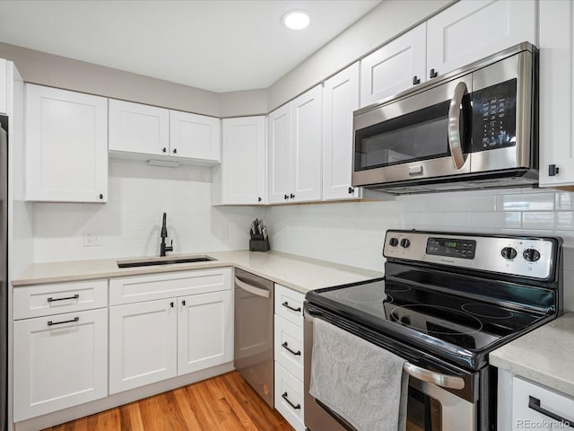 kitchen with stainless steel appliances, a sink, light countertops, white cabinets, and recessed lighting