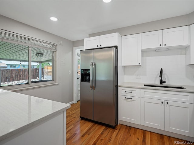 kitchen with stainless steel refrigerator with ice dispenser, a sink, white cabinetry, light wood-type flooring, and decorative backsplash