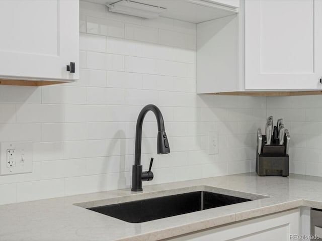 kitchen featuring decorative backsplash, a sink, white cabinetry, and light stone countertops