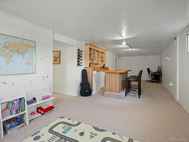 rec room with a dry bar, light colored carpet, rail lighting, and baseboards