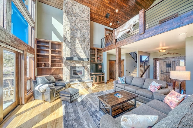 living area with wood ceiling, wood finished floors, stairs, a stone fireplace, and high vaulted ceiling