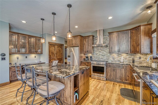 kitchen featuring a breakfast bar, appliances with stainless steel finishes, a sink, wall chimney range hood, and light wood-type flooring