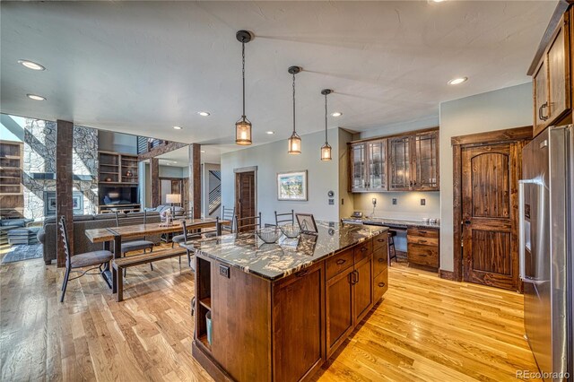 kitchen featuring light wood-style flooring, stainless steel fridge with ice dispenser, a center island, dark stone countertops, and decorative light fixtures