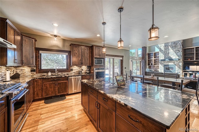 kitchen featuring light wood finished floors, decorative backsplash, appliances with stainless steel finishes, a sink, and dark stone countertops