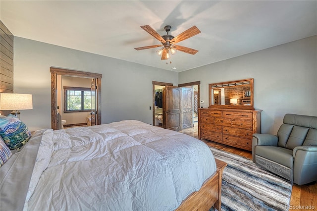 bedroom featuring ceiling fan, wood finished floors, and a walk in closet
